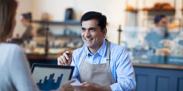 Smiling cafe worker talking to a customer with a tablet.