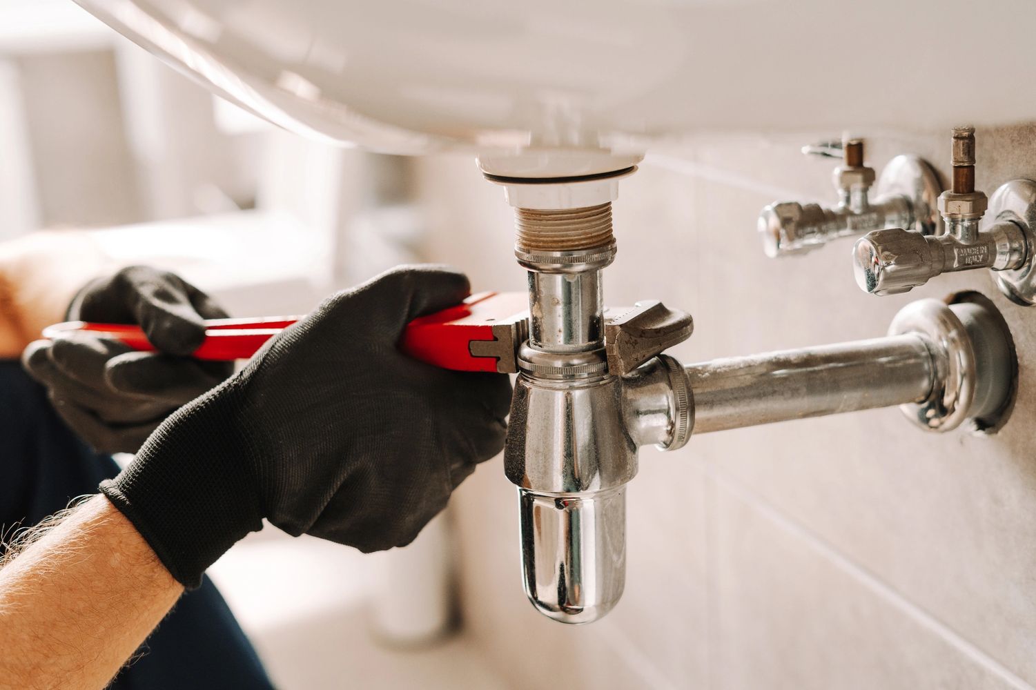 A plumber tightening a pipe under a sink with a wrench.