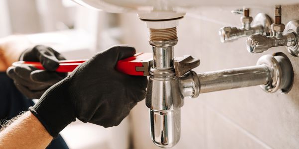 A plumber tightening a pipe under a sink with a wrench.