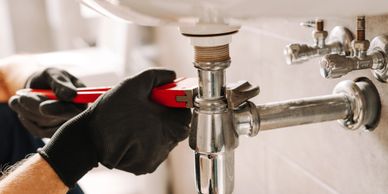 A plumber fixing a pipe under a sink with a wrench.