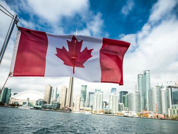 Canadian flag waving with Toronto skyline and CN Tower in background.
