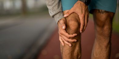 Person holding their knee in pain during outdoor exercise.