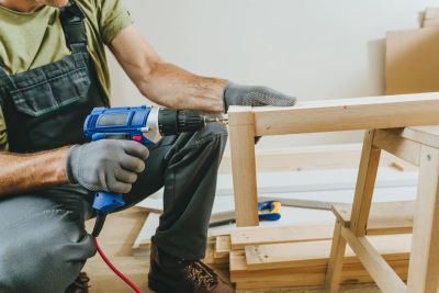 Person assembling wooden furniture with drill.