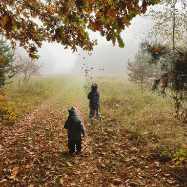 Two children play with falling leaves on a foggy autumn path.