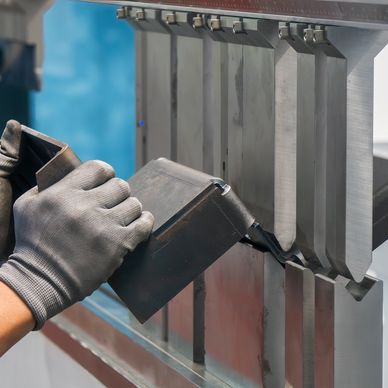 A worker wearing gloves operates a metal bending machine with precision.