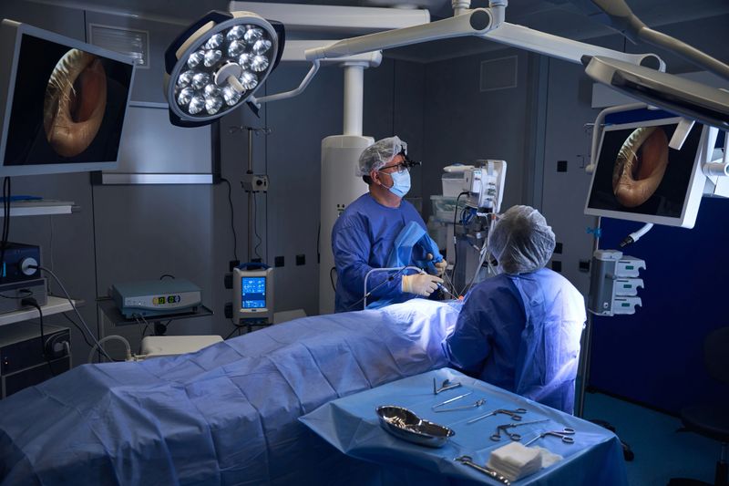 Two surgeons in sterile attire prepare surgical instruments under bright lights in a high-tech operating room