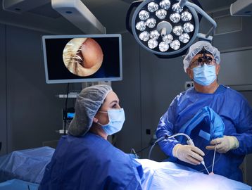 Surgeons performing a minimally invasive surgery with endoscopic guidance in an operating room.