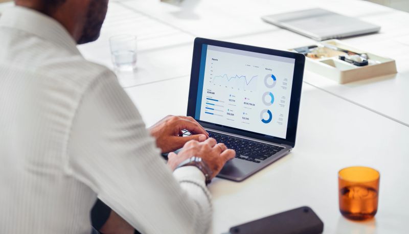 A businessman in a white shirt uses a laptop to analyze financial data and charts, focusing on business growth and strategy development in a modern office setting.