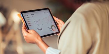 Person holding a tablet displaying financial reports and graphs.