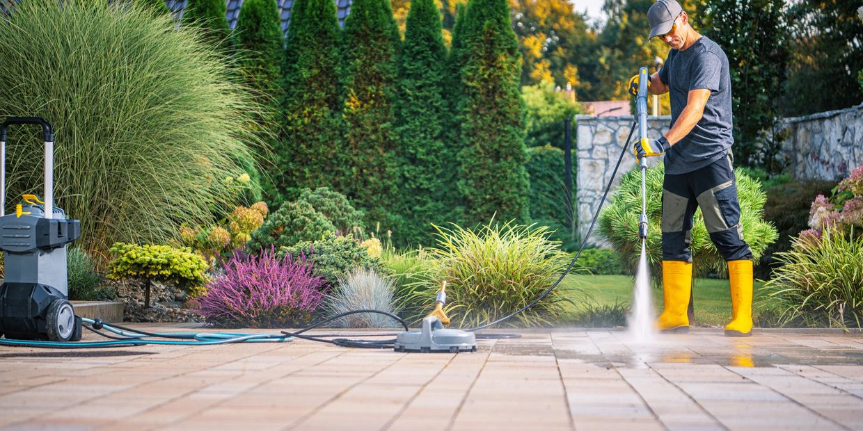 Power washing a brick patio among green bushes.