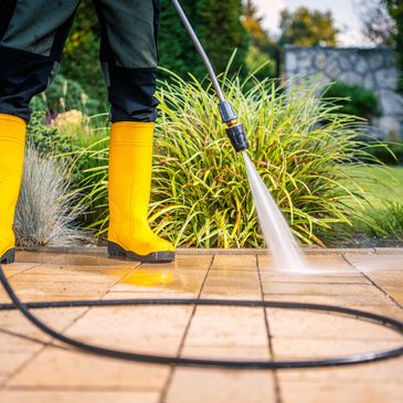 Person cleaning patio tiles with a pressure washer wearing yellow boots.