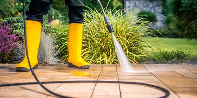 Person cleaning patio tiles with a pressure washer wearing yellow boots.