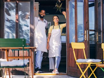 Two smiling cafe workers stand at the doorway wearing aprons.
