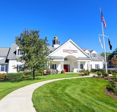 Town hall building with manicured lawn and flags under a clear blue sky.