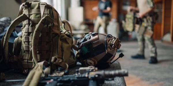 Military gear including helmet and backpack with blurred soldiers.