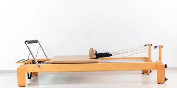 Wooden Pilates reformer machine on a white floor and wall.