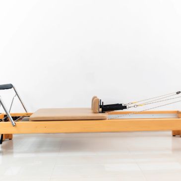 Wooden Pilates reformer with straps and padded platform.