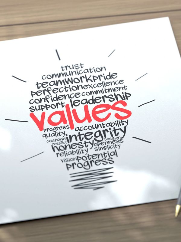 Paper with a lightbulb-shaped word cloud about values and a pen on a wooden table.