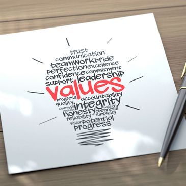 Paper with a lightbulb-shaped word cloud about values and a pen on a wooden table.