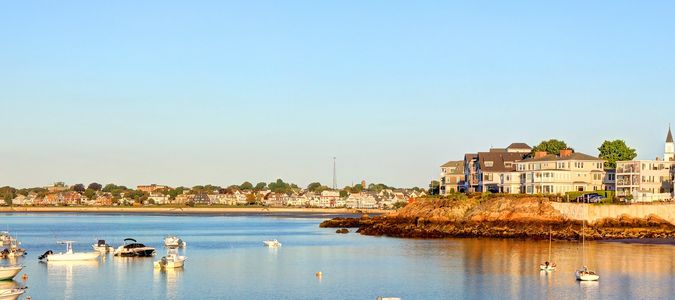 Calm harbor with boats and shoreline houses at sunset.