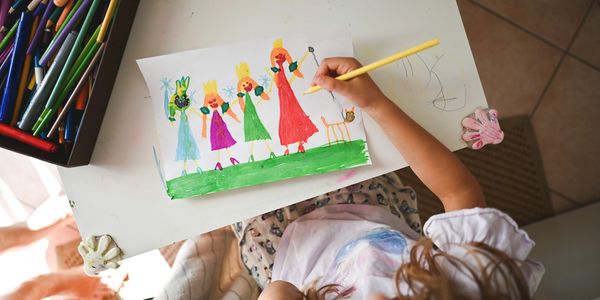 Child drawing colorful figures and a cat on paper with colored pencils.
