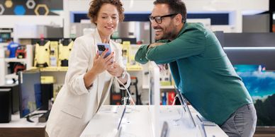 Two people happily discussing a smartphone in an electronics store.