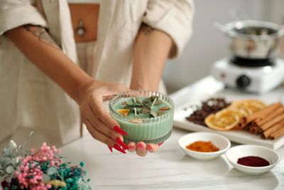 A person holding a green candle with dried flowers and herbs.