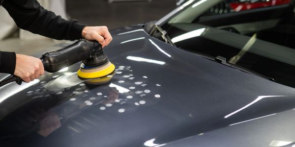 Person polishing a car's hood with a buffer machine.