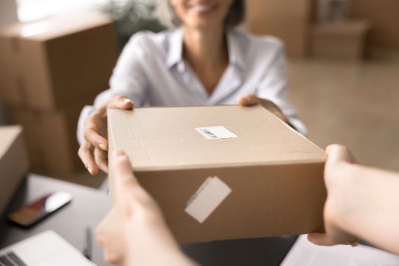 Close up crop view happy middle-aged businesswoman engaged in shipping or delivery process, handling parcel box ready for shipment to recipient. Logistical workflow, small business, selling and buying