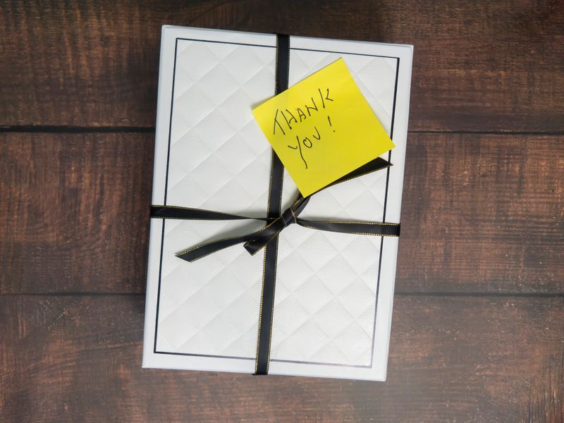Yellow Thank You Post-it Note on gift box with black ribbon on a wood background