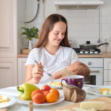 Mother feeding baby while eating breakfast.