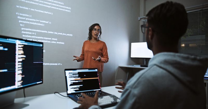 Hispanic Latin American software engineer developer use laptop computer program coding, projection screen presentation. Programming language development, business technology, night work people concept