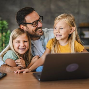 Father joyfully spending time with his two smiling daughters at a laptop.