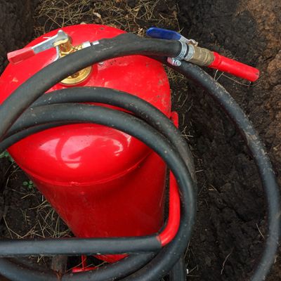 Red fire extinguisher with a black hose lying on dirt.