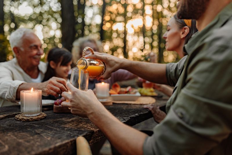 Family enjoying a picnic day in the woodland while father is pouring juice in a glass