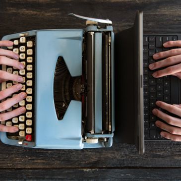Hands typing on typewriter and laptop side by side.