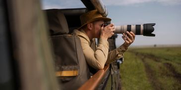 A man with a camera and telephoto lens takes photos from a safari vehicle.