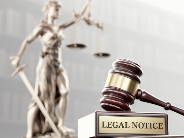 A gavel and legal notice plaque with Lady Justice statue blurred in background.