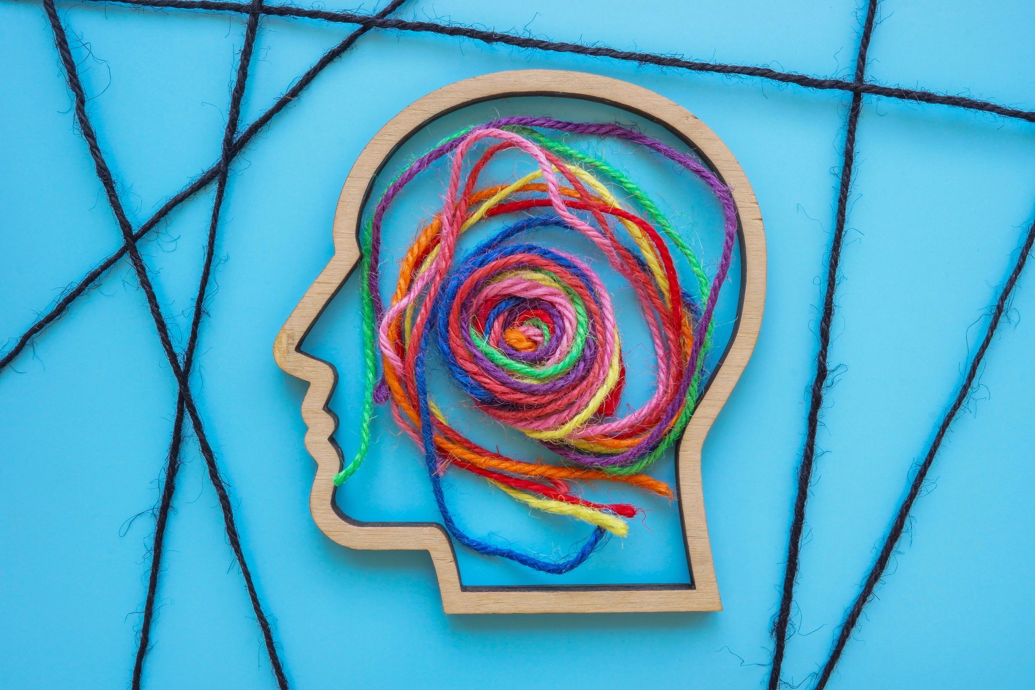 Wooden head outline with colorful yarn spiral inside on blue background.