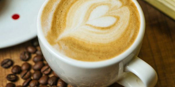 A cup of latte with heart-shaped latte art and coffee beans scattered nearby.