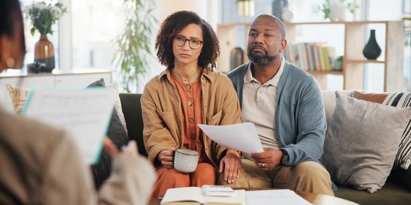 Concerned couple discussing documents with a professional in a cozy living room.