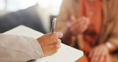 Person writing notes in a notebook during a conversation.