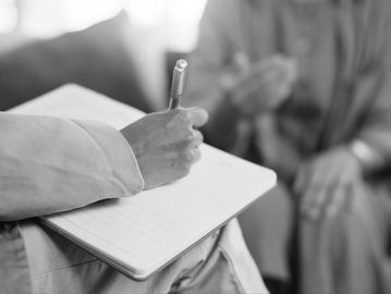 Person writing notes in a notebook during a conversation.