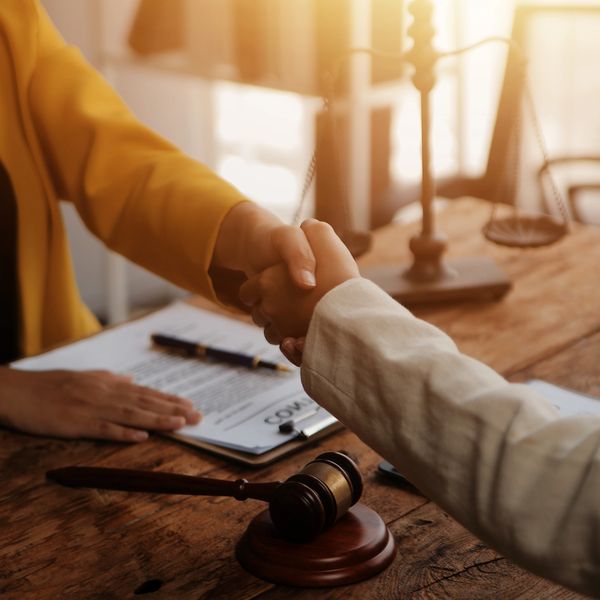 Two people shaking hands over a legal document with a gavel on the table.