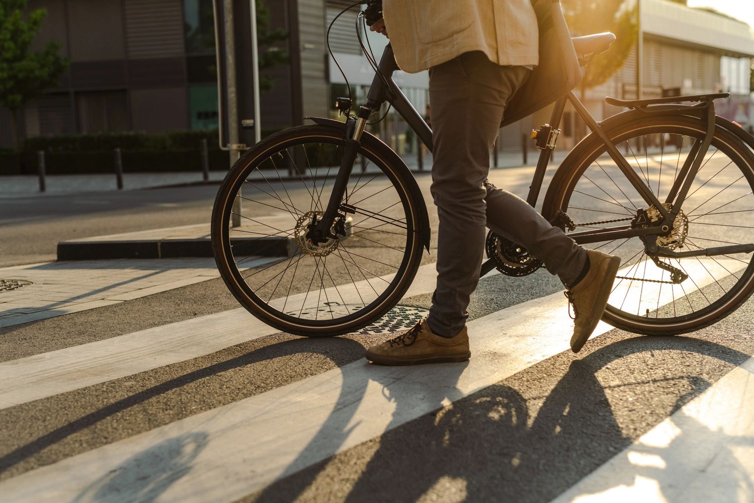 Person walking a bicycle on a sunlit city street crossing.