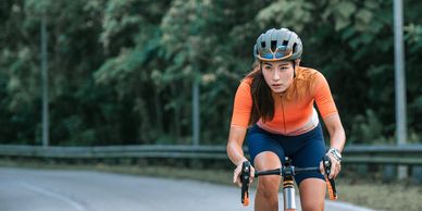 Focused female cyclist riding on a winding road surrounded by greenery.