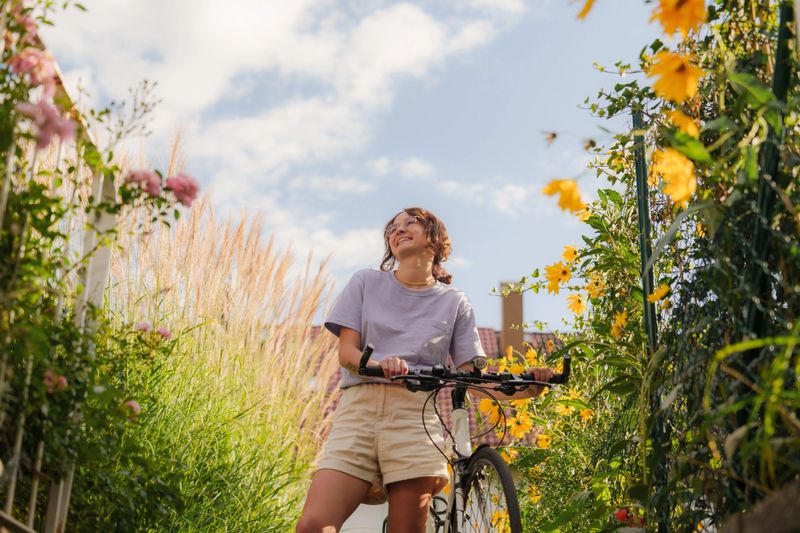 Woman with bicycle among flowers on backyard on sunny day
