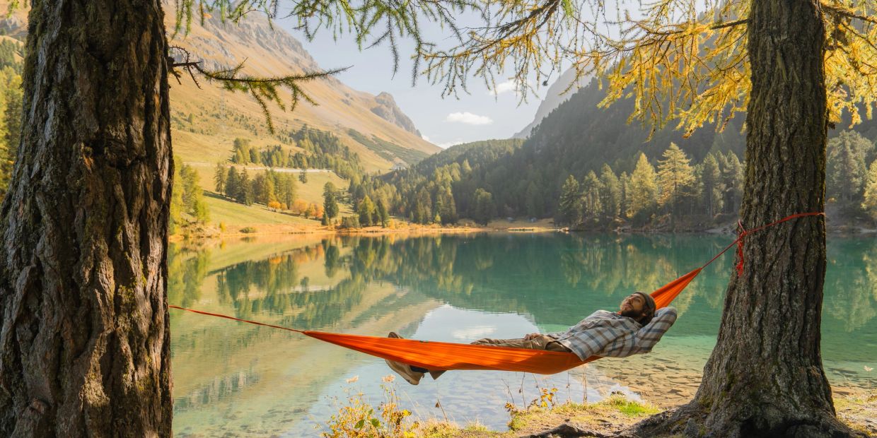 Hombre relajándose en hamaca junto a lago en el bosque.