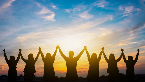 Silhouettes of people holding hands at sunset, symbolizing unity and strength.
