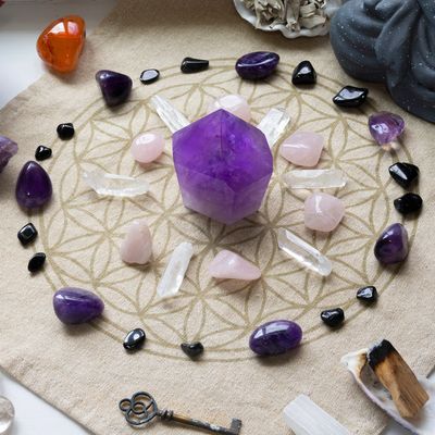 A crystal grid with a central purple amethyst surrounded by various stones and a key.